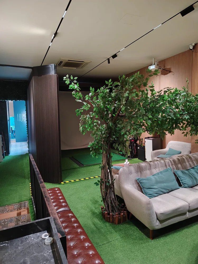 Wide view of the AnyBirdie lounge, projector and simulator screen over turf flooring