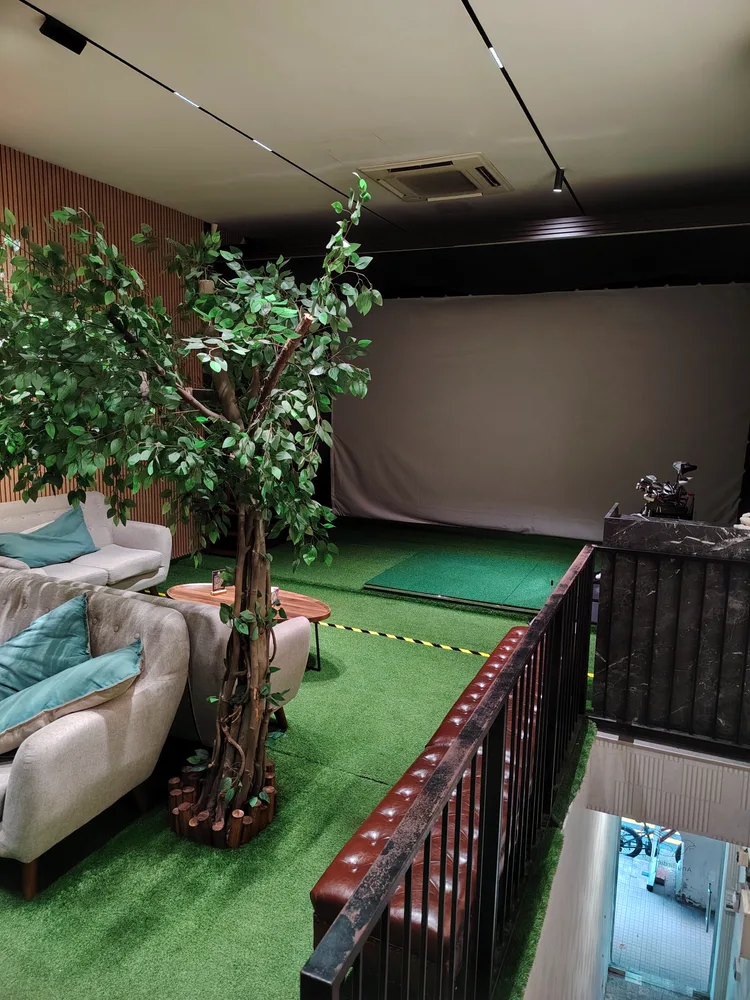 AnyBirdie lounge with sofas and indoor tree beside the simulator hitting mat